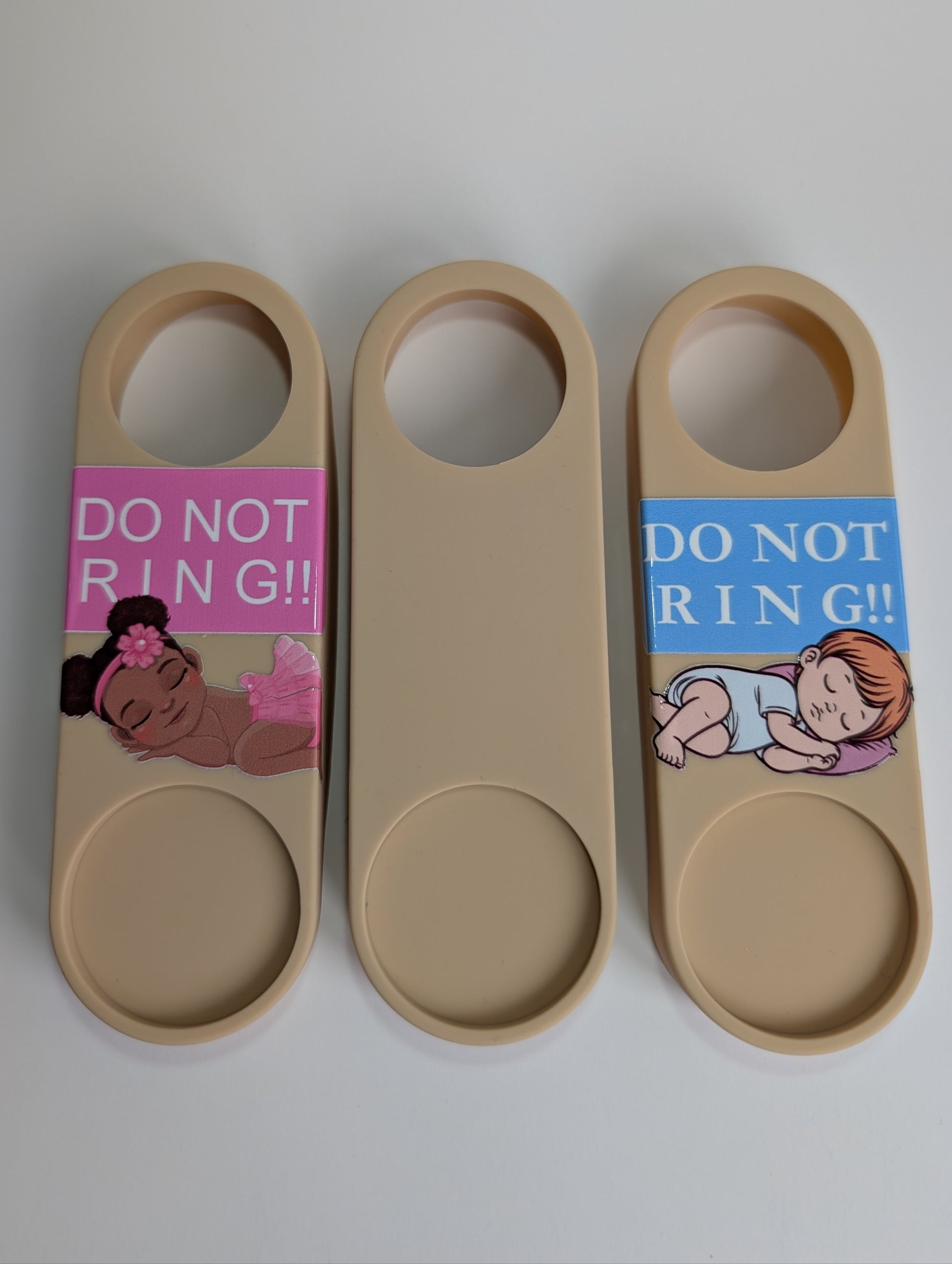 Three beige door openers with baby-themed labels on a gray background